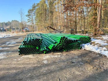 Kanalizasyon şebekesinin inşası sırasında yol kenarında depolanan yeşil ve kahverengi kanalizasyon boruları.