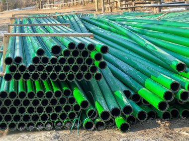 Kanalizasyon şebekesinin inşası sırasında yol kenarında depolanan yeşil ve kahverengi kanalizasyon boruları.