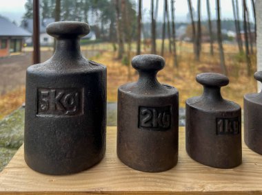 Eski döküm demir ağırlıklar arka planda bir köy ve seyrek bir orman.