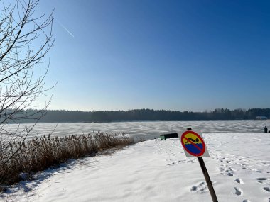 Kışın donmuş bir gölde yüzmeyi yasaklayan bir tabela, karla kaplı bir plajda..
