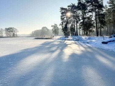 Donmuş bir gölün üzerinde yürüyen bir patika tarafından karla kaplı bir bank..