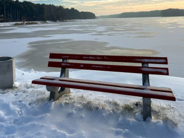 Donmuş bir gölün üzerinde yürüyen bir patika tarafından karla kaplı bir bank..