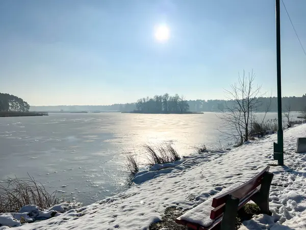 Donmuş bir gölün üzerinde yürüyen bir patika tarafından karla kaplı bir bank..