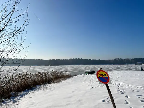 Kışın donmuş bir gölde yüzmeyi yasaklayan bir tabela, karla kaplı bir plajda..