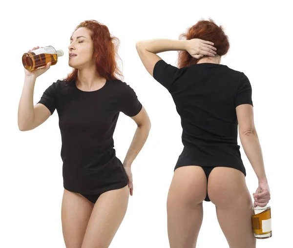 照片上是一个年轻美丽的红头发女人 穿着空白的黑色衬衫和黑色内裤 喝着瓶子里的威士忌 与白色背景隔离 并准备好为您的设计或艺术品 免版税图库照片
