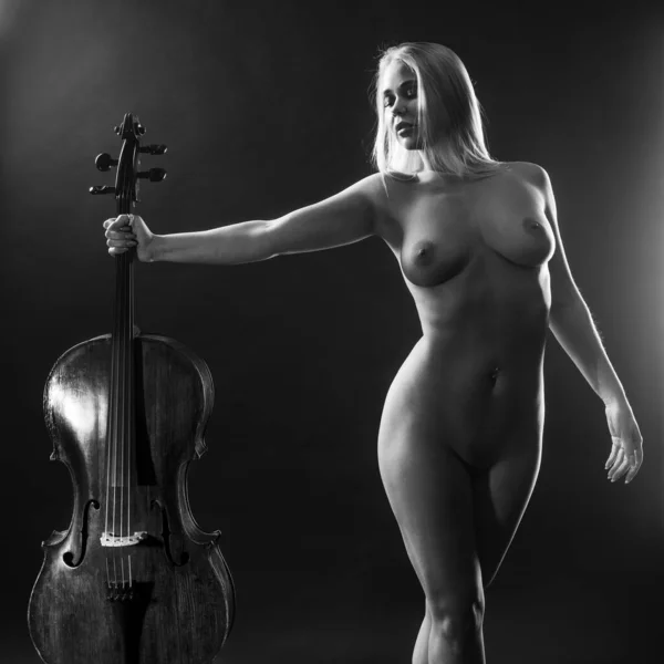 stock image Gorgeous nude blond woman standing with an old cello over black background.