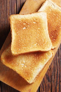 Mutfak tahtasının üzerinde kızarmış ekmek dilimleri. Ahşap masa. Yakın çekim, üst manzara.