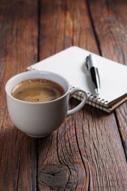 Bir fincan kahve ve eski ahşap masadaki kalemli not defteri.