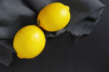 Two yellow lemons on black stone background, top view with copy space