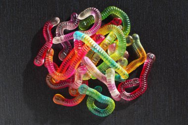 Heap of bright colorful jelly worms on black stone background, top view