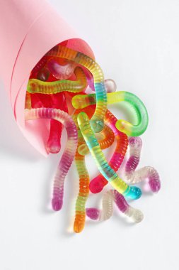 Colorful jelly worms in pink paper bag on white background