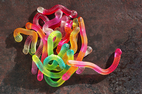 Heap of bright colorful jelly worms on grunge metal background, top view