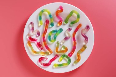 Pembe arka planda bir tabakta renkli jelibon solucanlarının üst görüntüsü