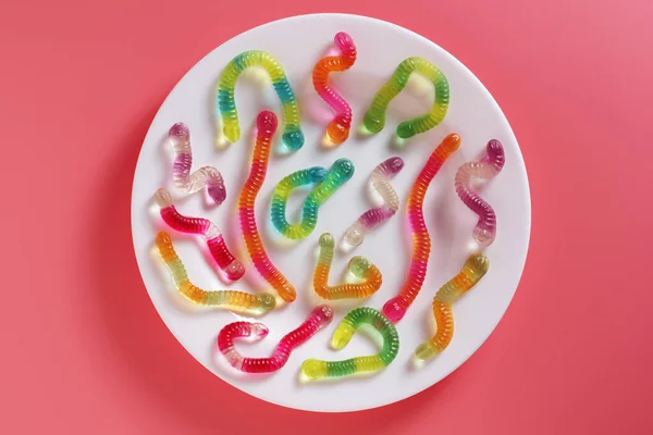 粉色背景的盘子上彩色粘性蠕虫的顶部视图 — 图库照片