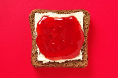 Kırmızı arka planda çilek reçelli küçük çavdar ekmeği dilimi.