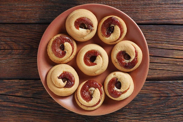 Shortbread cookies with jam on a brown plate on wooden background, top view