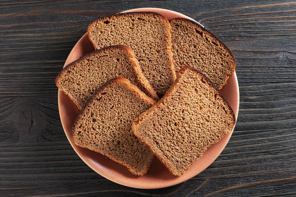 黒い木の背景に皿の上にスライスしたライ麦パン トップビュー — ストック写真