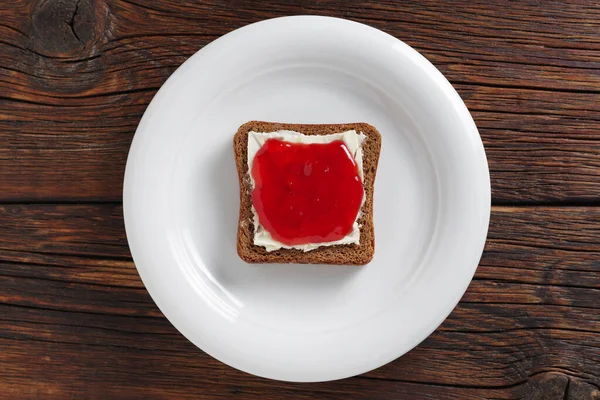木製の背景に皿の上にイチゴジャムと小さなライ麦パンのスライス トップビュー — ストック写真