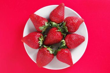 Kırmızı arka planda bir tabakta çilek, üst manzara