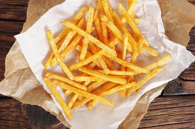 Ahşap arka planda buruşmuş kağıt üzerinde patates çubukları yığını, üst manzara.