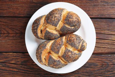 Ahşap bir tabakta haşhaş tohumlu küçük örülmüş çörekler.