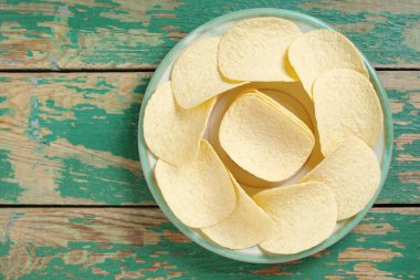 Eski yeşil ahşap arka planda, tabakta tuzlu patates cipsleri, fotokopi alanı olan üst manzara. Bira için iyi atıştırmalık