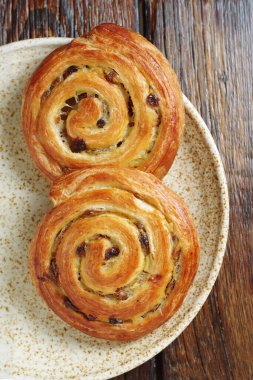 Kuru üzümlü börekler eski ahşap arka planda bir tabakta yuvarlanıyor.