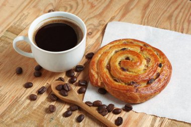 Eski ahşap arka planda bir fincan kahve ve kuru üzümlü börek.