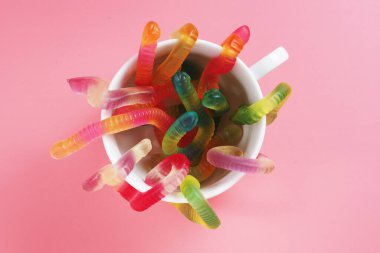 Pembe arka planda beyaz bardaktaki renkli solucanların üst görüntüsü. Çiğnenmiş meyve şekeri