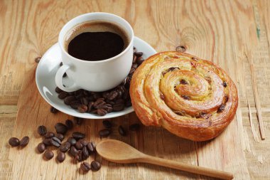 Eski ahşap arka planda bir fincan kahve ve kuru üzümlü börek.