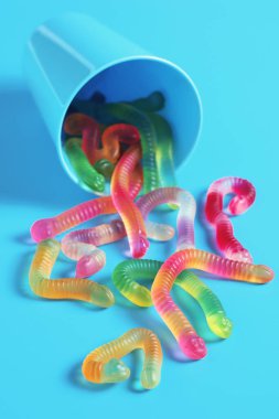 Renkli jelibon solucanlar plastik bir bardaktan mavi bir arka plana döküldü.