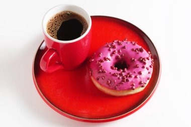 Şeker toplu pembe çörek ve beyaz arka plandaki kırmızı çatal bıçaklara bir fincan kahve.