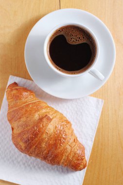 Bir fincan kahve ve ahşap bir masada taze kruvasan.