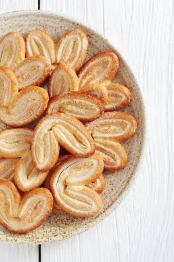 French Palmiers Cookies - Elephant Ear cookies in a plate on white wooden background, top view clipart