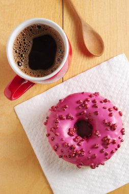 Şeker topları serpiştirilmiş pembe çörek ve ahşap arka planda kırmızı bir fincan kahve. 