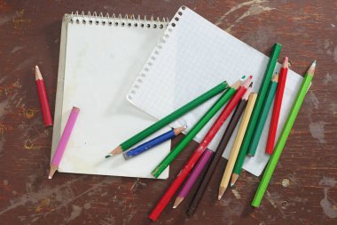 Not defteri ve kirli bir ofis masasında bir sürü farklı kalem, üst görünüm.