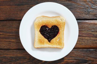 Kalp şeklinde kesilmiş tost ekmeği eski bir ahşap masada kuşüzümü reçeli ile yapılır. Yukarıdan görüntüle