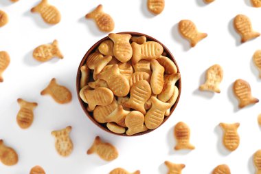 Beyaz arka planda tahta bir kasede balık şeklinde krakerler.