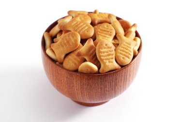 Beyaz arka planda tahta bir kasede balık şeklinde krakerler.