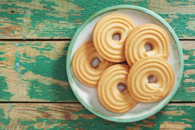 Eski yeşil ahşap zemin üzerinde bir tabak içinde küçük ekmek halka kurabiyeleri, kopya alanı ile üst görünüm