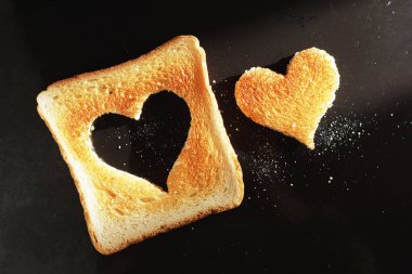 Kadeh kaldırırken kalp şeklinde kesikler ve kırıntılar, arka planda siyah tepsi, üst görünüm