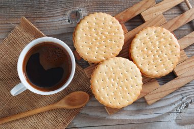 Bir fincan kahve ve ahşap arka planda yuvarlak sandviç kurabiyeleri.