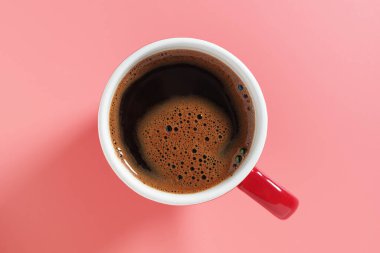 Pembe arka planda kırmızı bardakta bir fincan kahve, üst manzara.