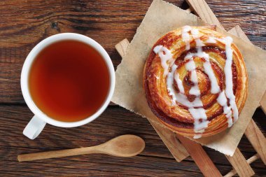 Kremalı tarçınlı çörek tomarı ve eski ahşap masada bir fincan çay.
