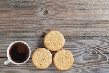 Bir fincan kahve ve ahşap arka planda yuvarlak sandviç kurabiyeleri, fotokopi alanı olan üst manzara.