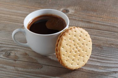 Bir fincan kahve ve ahşap arka planda yuvarlak sandviç kurabiyesi.