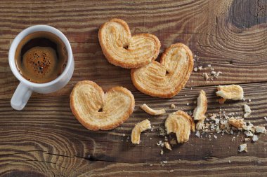 Bir fincan kahve ve kırık palmiyeler ahşap arka planda poğaça kurabiyeleri, üst manzara.