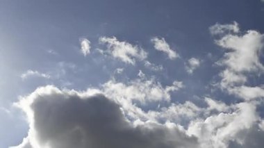 White and gray autumn clouds cross the sky from top left to bottom right. Blue sky, sunny afternoon with cumulus clouds passing quickly. Low-angle timelapse view.