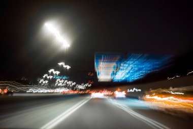 Gece otobanında arabalar, işaretler ve ışıklar, uzun pozlu fotoğrafçılığın yarattığı hareket bulanıklığı.