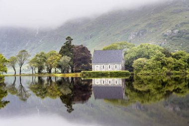 Sakin suya yansıyan küçük bir kilise. St. Finbarr 'ın hatipliği İrlanda' nın Gougane Barra gölündeki bir adada yer almaktadır..